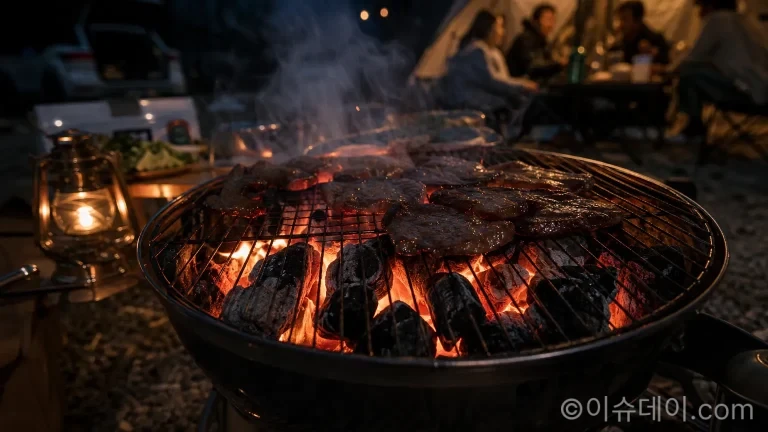활활 타오르는 캠핑용 숯불 위에 고기가 구워지고 있는 모습.